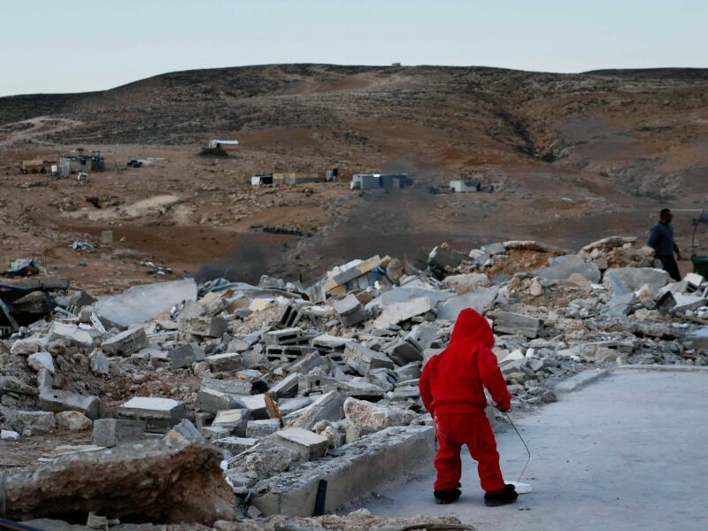 ​A child wearing red stands amidst rubble in a desolate field