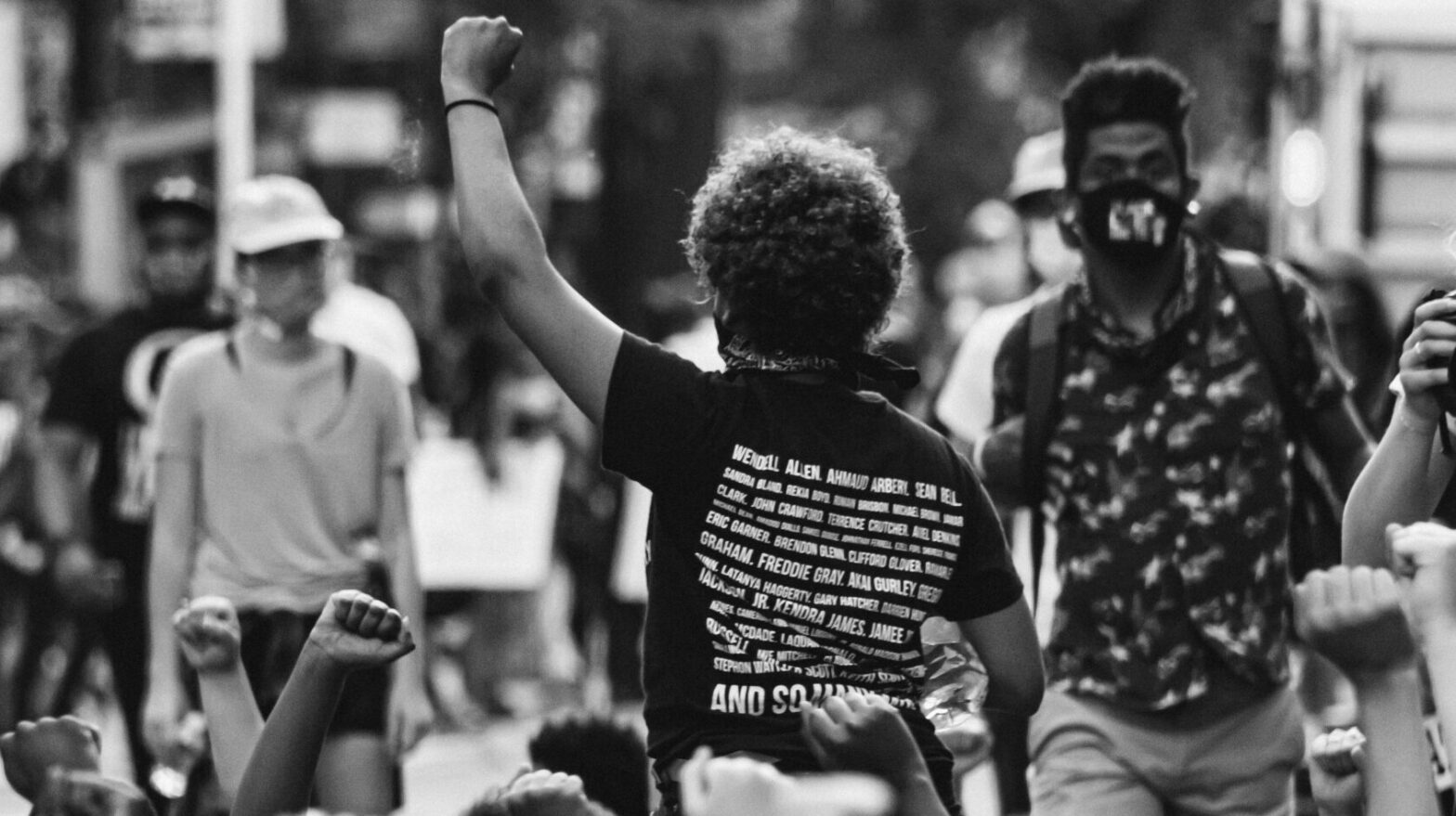A crowd of demonstrators raise their fist in protest. The image is black and white.