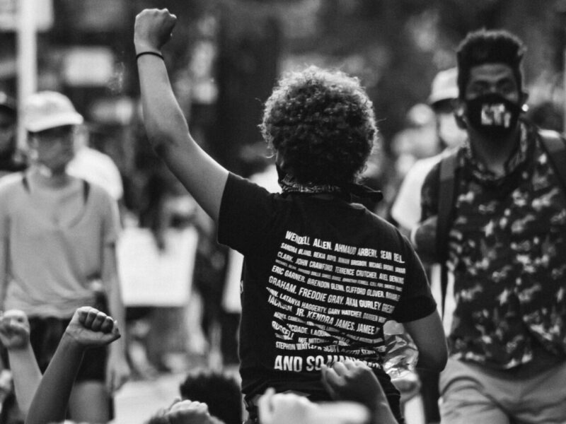 A crowd of demonstrators raise their fist in protest. The image is black and white.