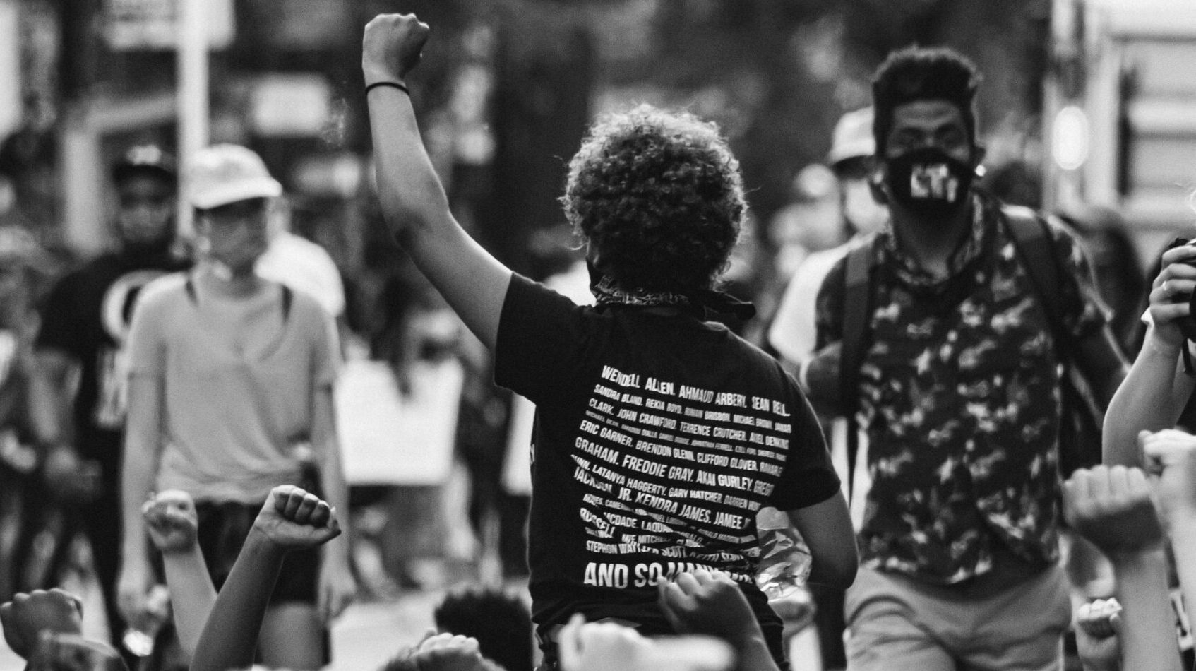A crowd of demonstrators raise their fist in protest. The image is black and white.