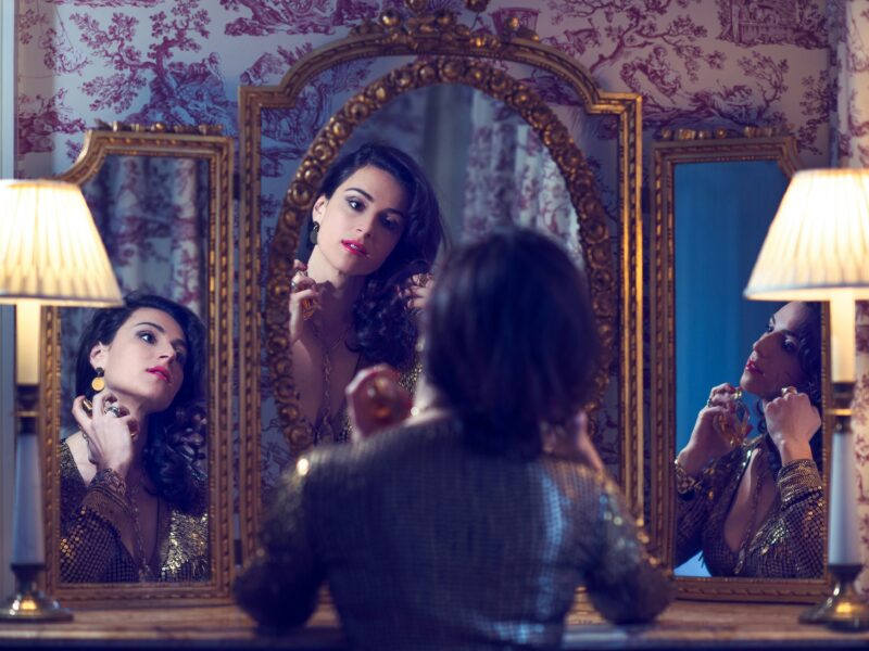 Photo of a woman applying make up in front of a mirror.