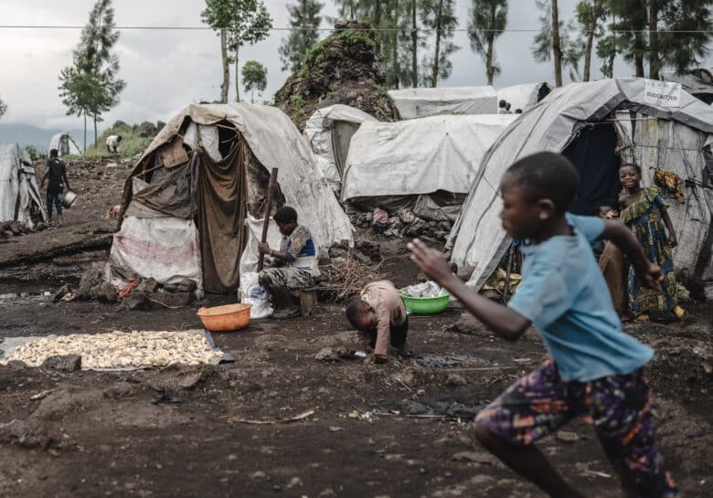 A displaced woman(C) mashes cassava in front of a tent in the internally displaced persons camp, home to tens of thousands of war-displaced people, on the outskirts of Goma, eastern Democratic Republic of the Congo, on April 11, 2024.