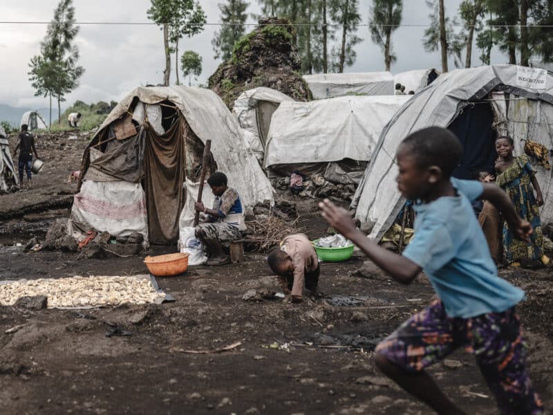 A displaced woman(C) mashes cassava in front of a tent in the internally displaced persons camp, home to tens of thousands of war-displaced people, on the outskirts of Goma, eastern Democratic Republic of the Congo, on April 11, 2024.