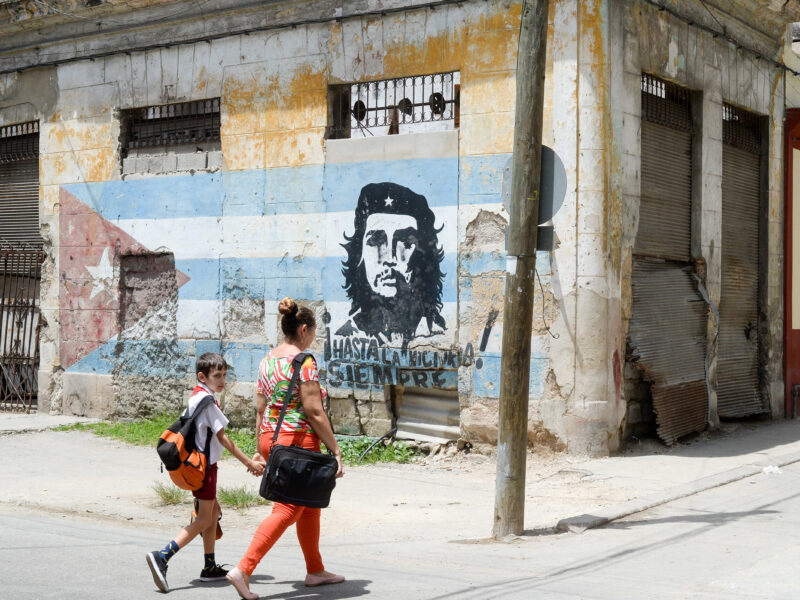 Passers-by walking by graffiti of Che Guevara on a Cuban flag at a street corner in old town Havana on June 22, 2018.