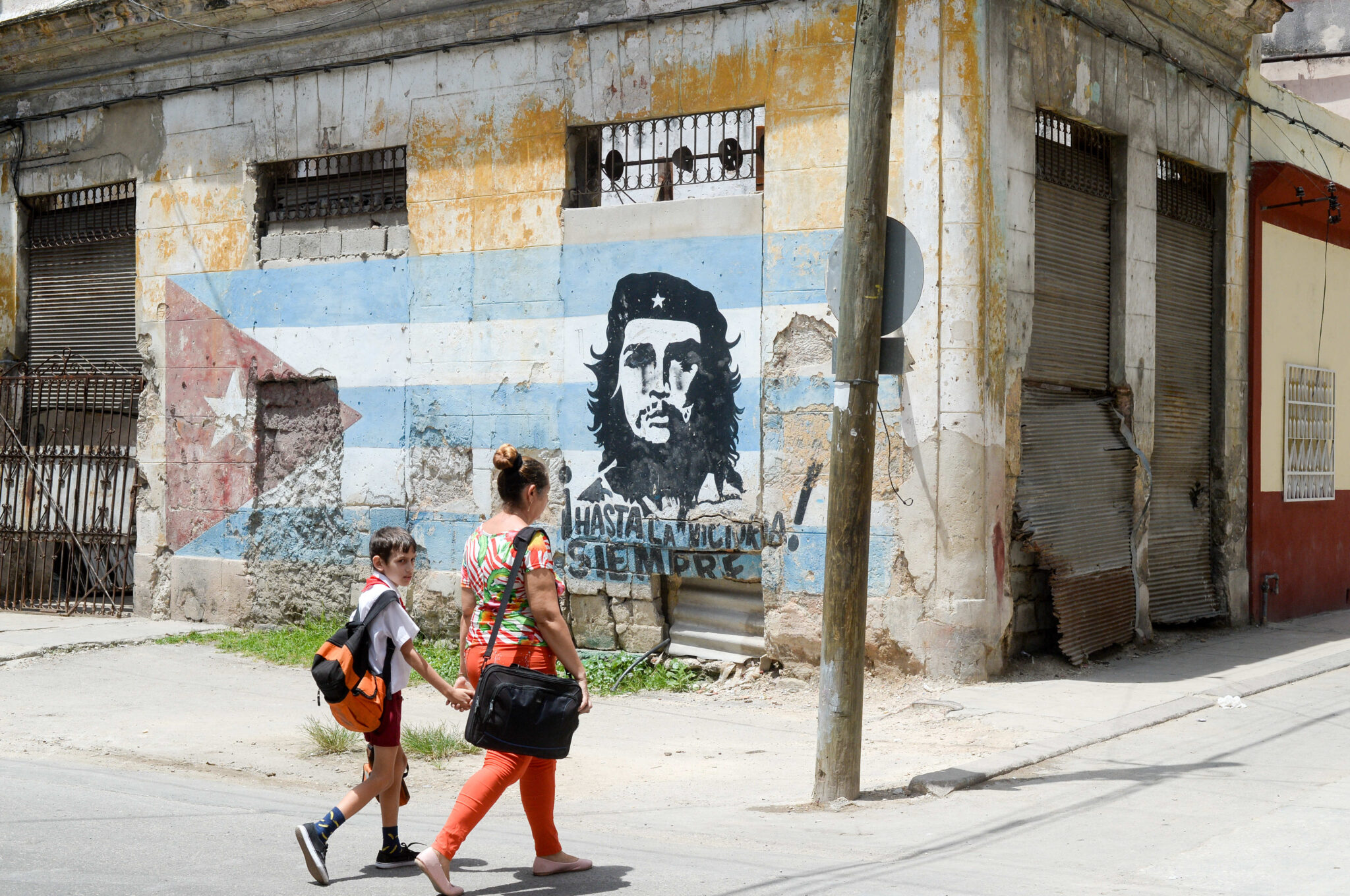 Passers-by walking by graffiti of Che Guevara on a Cuban flag at a street corner in old town Havana on June 22, 2018.