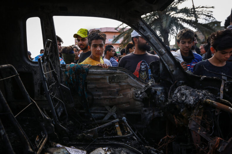 People inspecting a vehicle destroyed by an explosive device at a street market in the City of Sadr in eastern Baghdad, which killed at least one civilian and injured 12 on April 15, 2021, in Baghdad, Iraq.