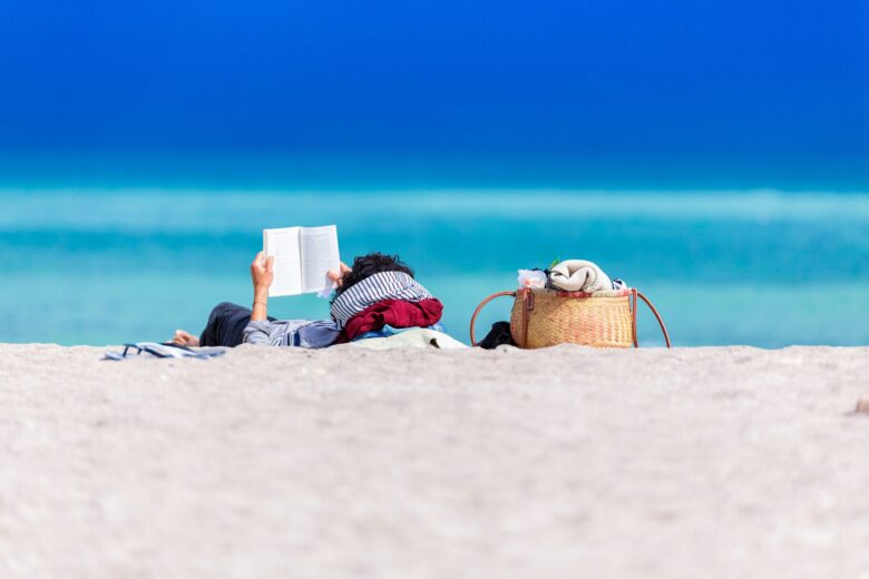A person lies on the beach reading a book