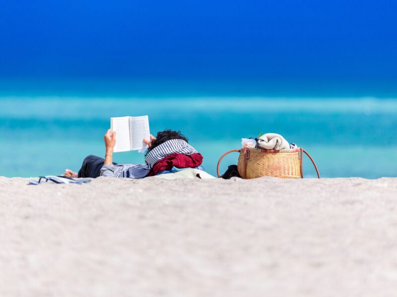 A person lies on the beach reading a book