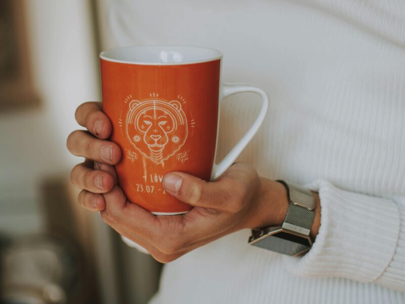 Person holding a cup decorated with an astrological sign graphic