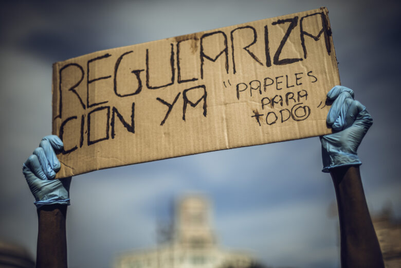 A migrant domestic worker protests for documents and regulation holding a placard reading 'regulation now. papers for all'