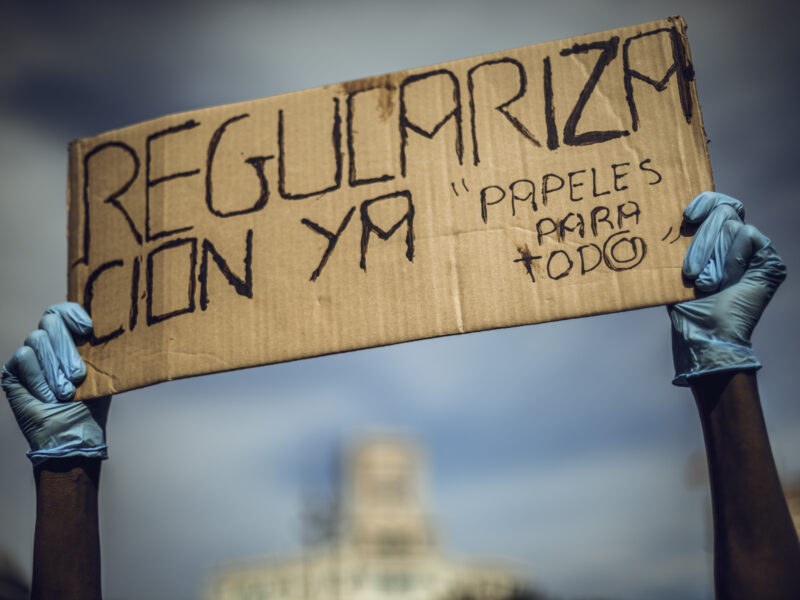 A migrant domestic worker protests for documents and regulation holding a placard reading 'regulation now. papers for all'