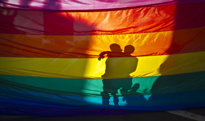 June 26, 2013 - San Diego, California, U.S - A couple hugs on the other side of a huge Pride flag, celebrating two decisions by the US Supreme Court seen as victories for gay marriage rights