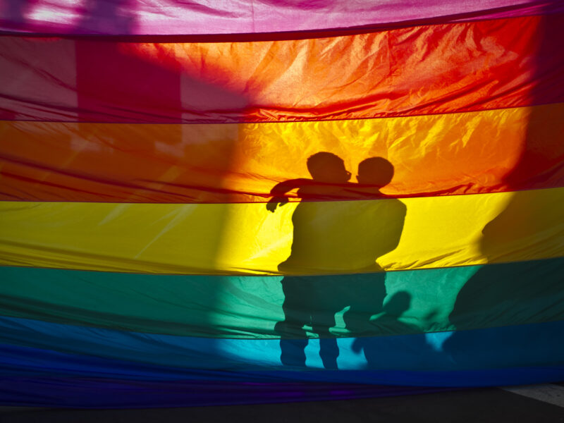 June 26, 2013 - San Diego, California, U.S - A couple hugs on the other side of a huge Pride flag, celebrating two decisions by the US Supreme Court seen as victories for gay marriage rights