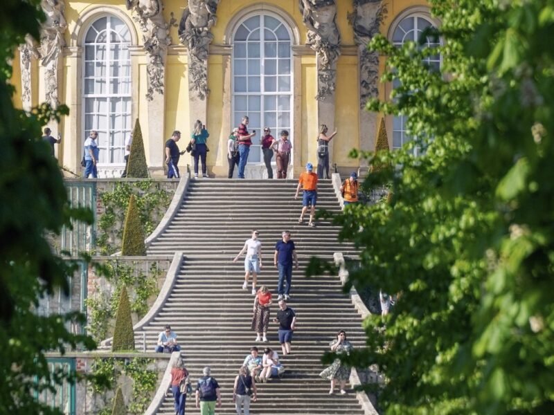People seated and walking on the steps of Sanssouci Palace, Potsdam, Germany.