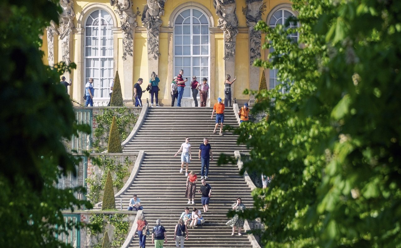 People seated and walking on the steps of Sanssouci Palace, Potsdam, Germany.