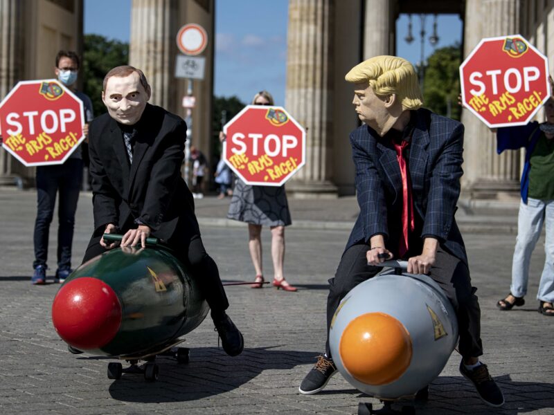 Two activists dressed as US President Trump and Russian President Putin ride two models of nuclear bombs in front of the Brandenburg Gate during a demonstration.