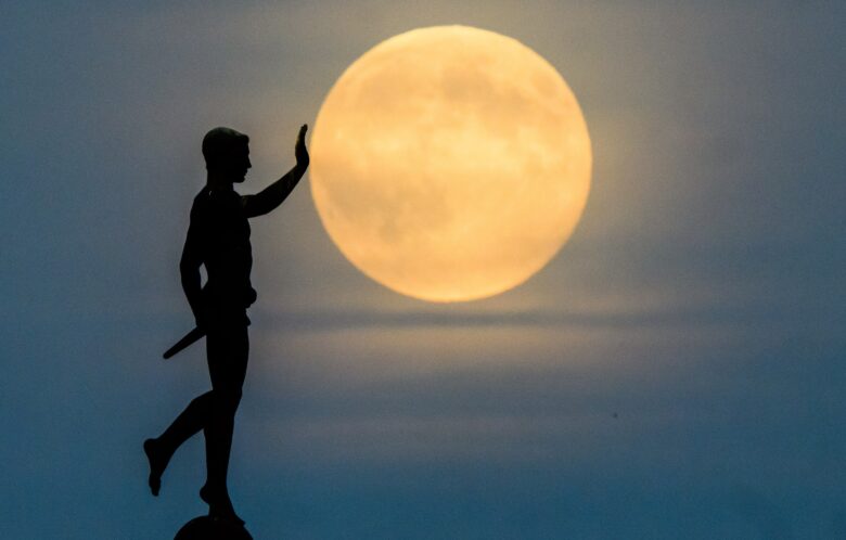 The moon rises on the horizon behind the ''Torchbearer'' statue (1937) on the northern shore of the Maschsee. 05 November 2025, Lower Saxony, Hanover.