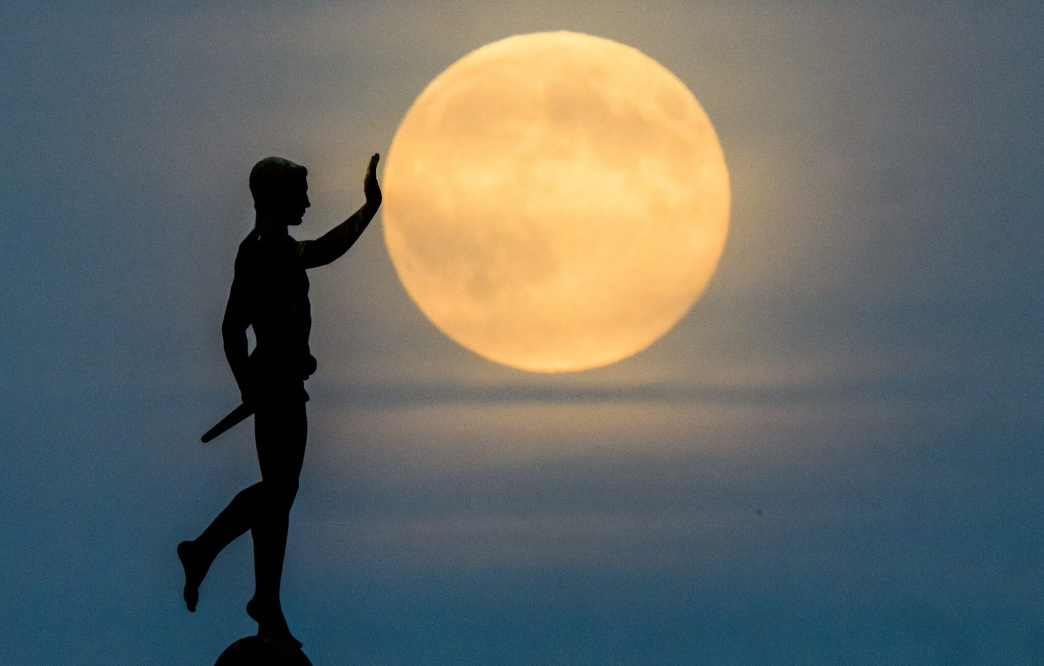 The moon rises on the horizon behind the ''Torchbearer'' statue (1937) on the northern shore of the Maschsee. 05 November 2025, Lower Saxony, Hanover.