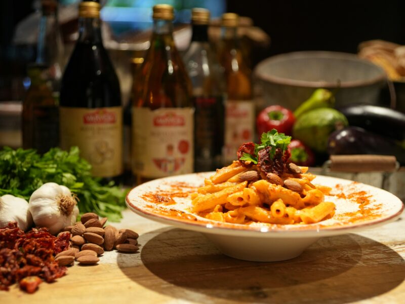 A plate of pasta on a table next to bottles of wine.