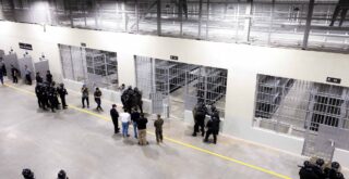 從俯瞰主要中心區域的走道上可以看到一座大型開放式監獄，其中設有禁區。身著防暴裝備的男子聚集在房間周圍。